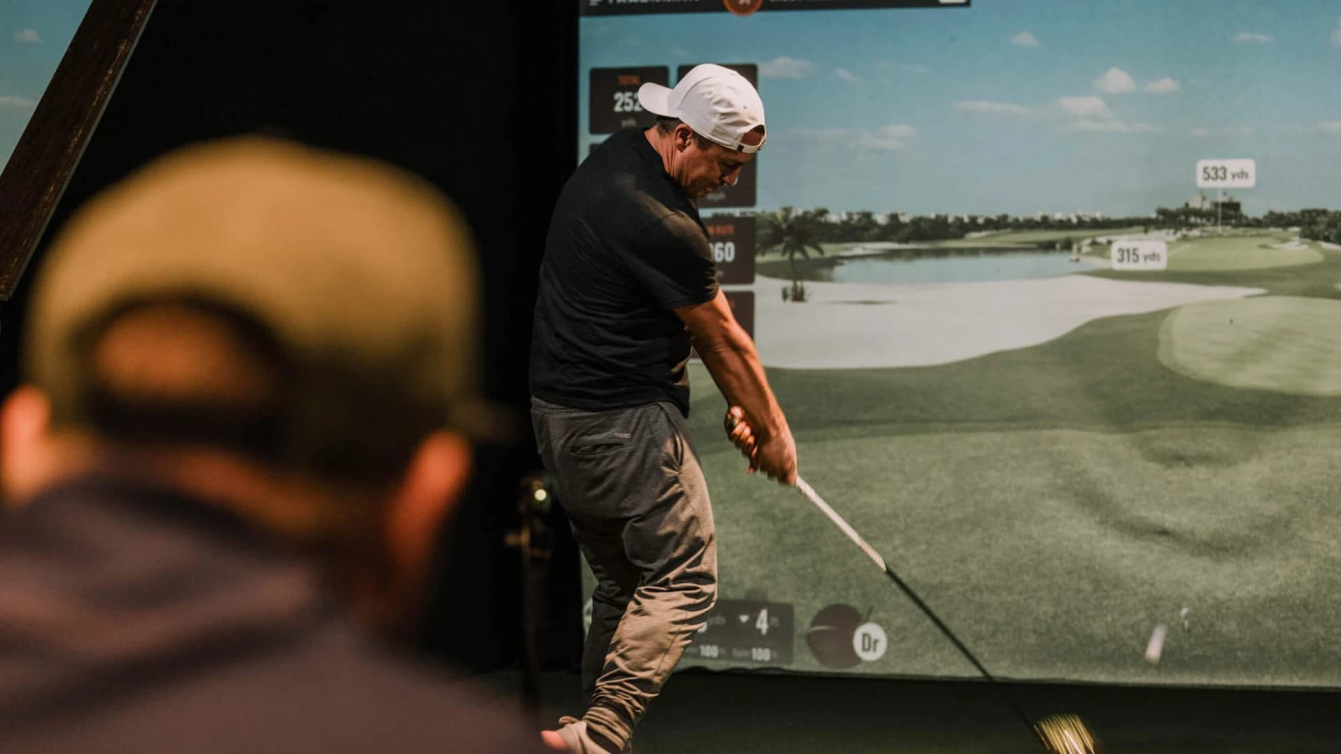 Golfer using SkyTrak+ simulator with data overlay on screen